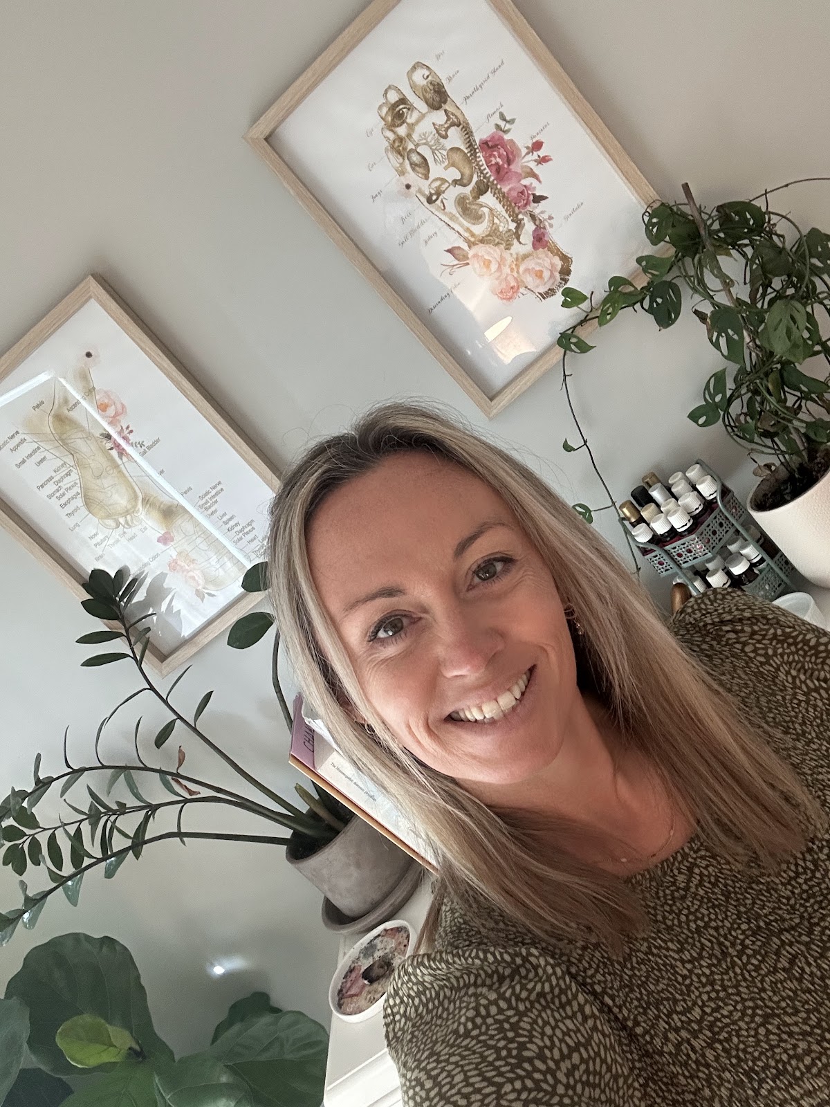 Alissia smiling in her treatment room, under her framed reflexology foot charts